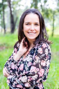 Smiling woman in a floral dress standing in a sunlit park